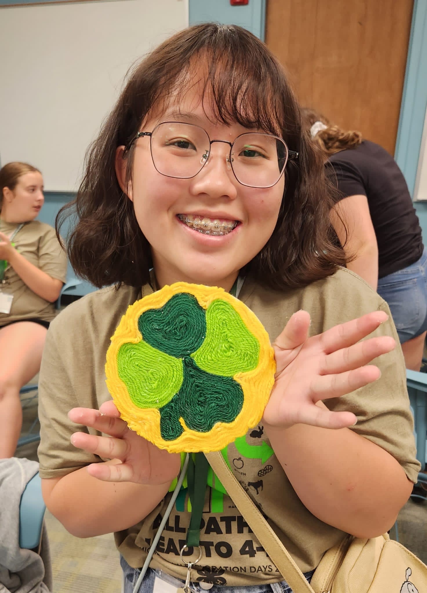 International guest from Taiwan 4-H proudly showing her artwork of green clover leaves on a yellow background.